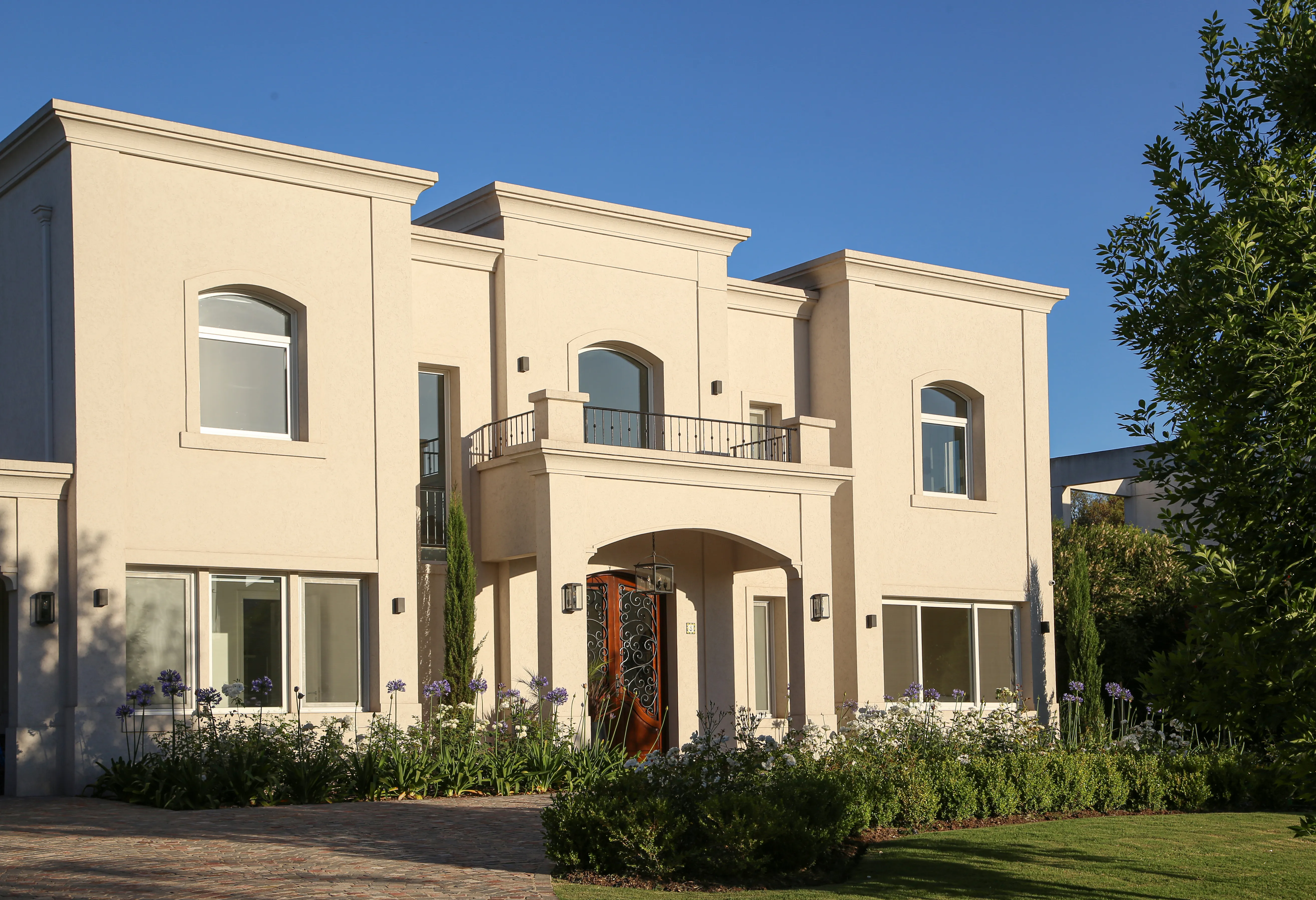 Casa cream stucco de día con jardín de agapanthus