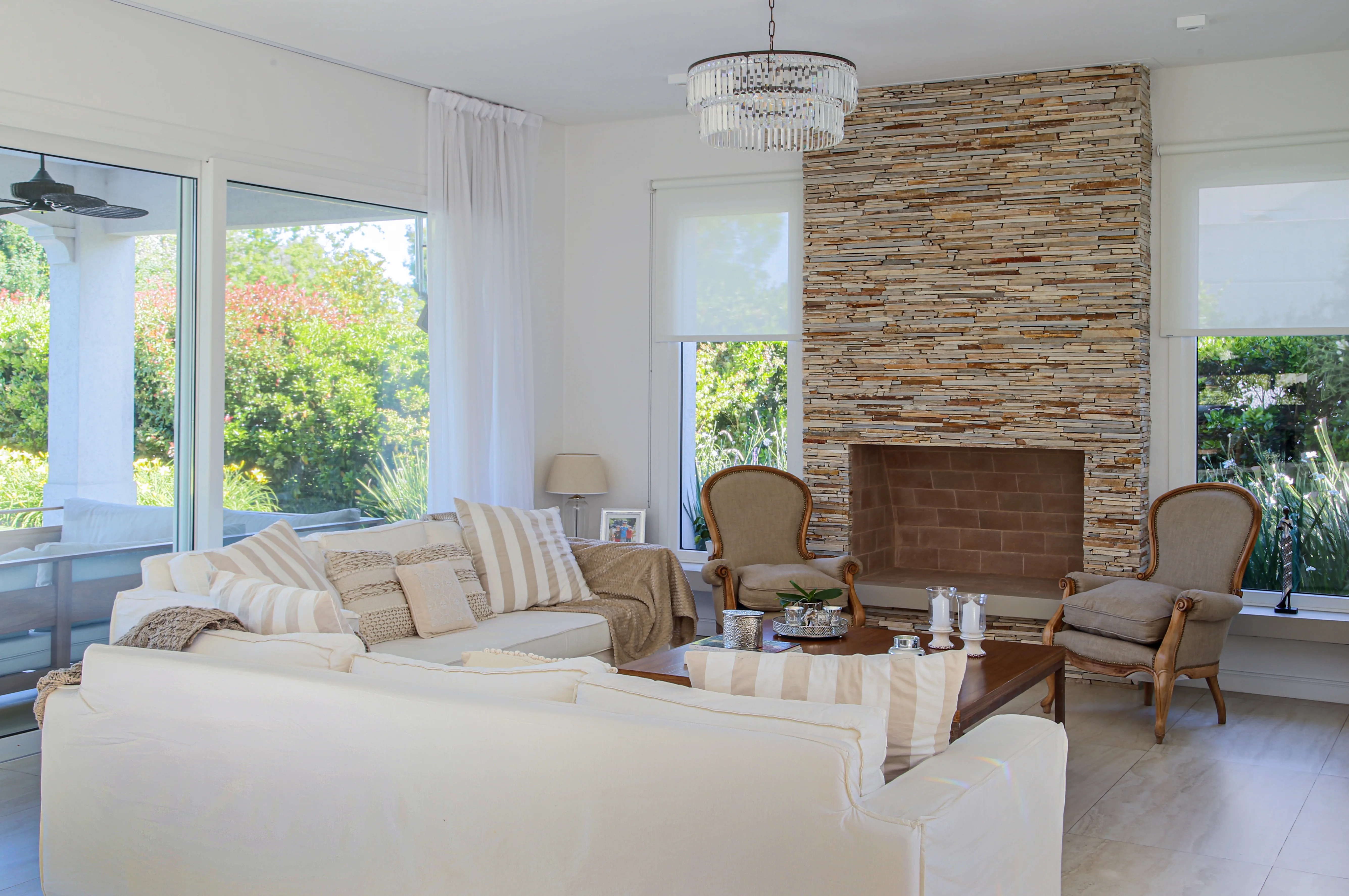 Living de una casa del estudio con chimenea de piedra, sillas francesas y paleta neutra en luz natural