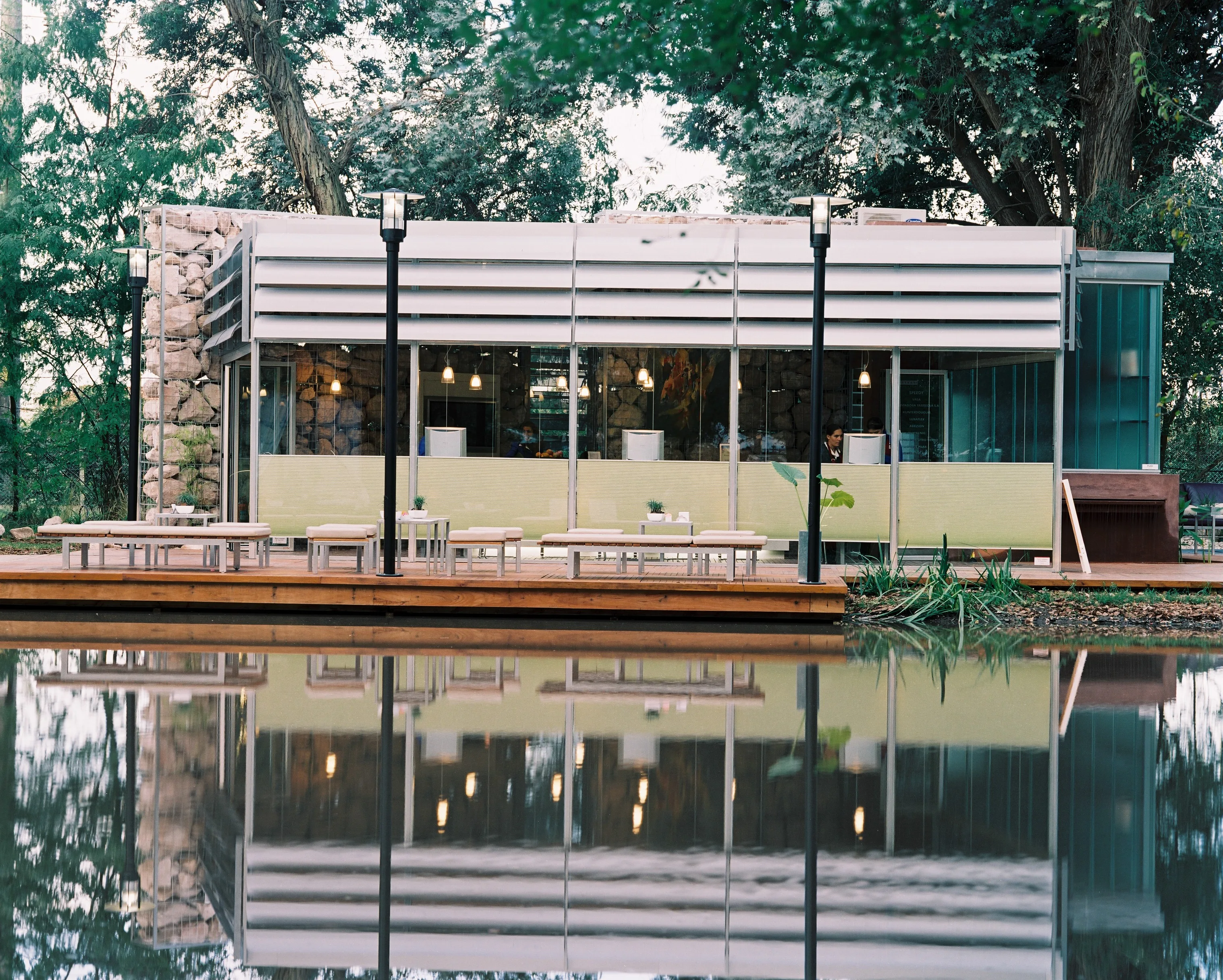 Quincho con estructura de vidrio reflejado en el agua, espacio exterior diseñado por el estudio