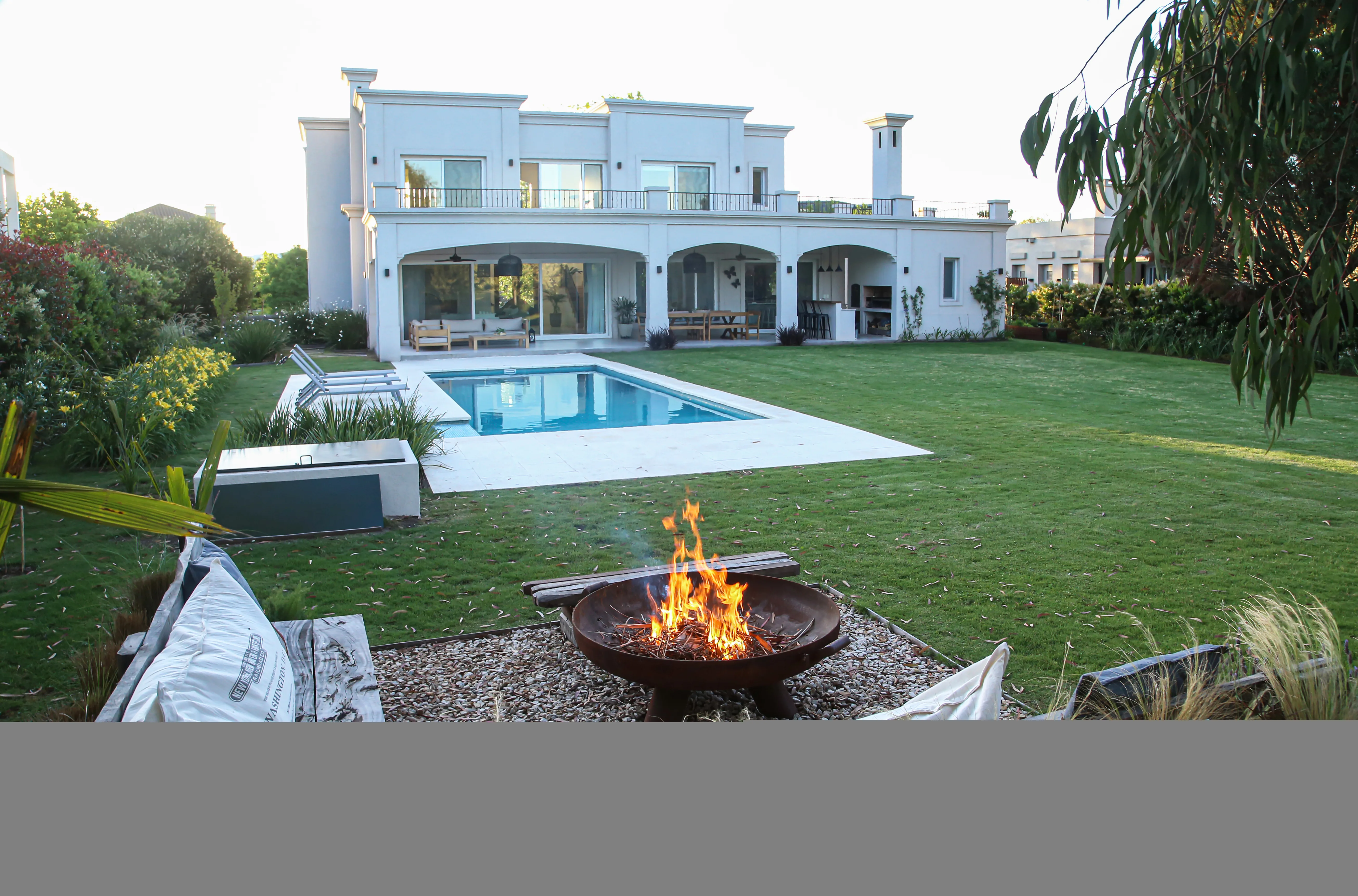 Casa blanca de estilo clásico con pileta y fogonero en primer plano, en un country de zona norte